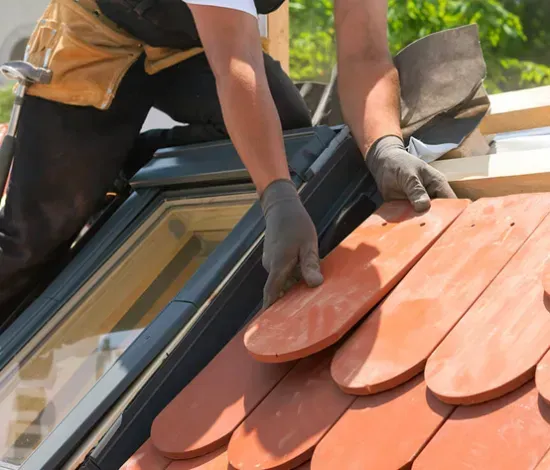 A man is laying tiles on a roof with a window.