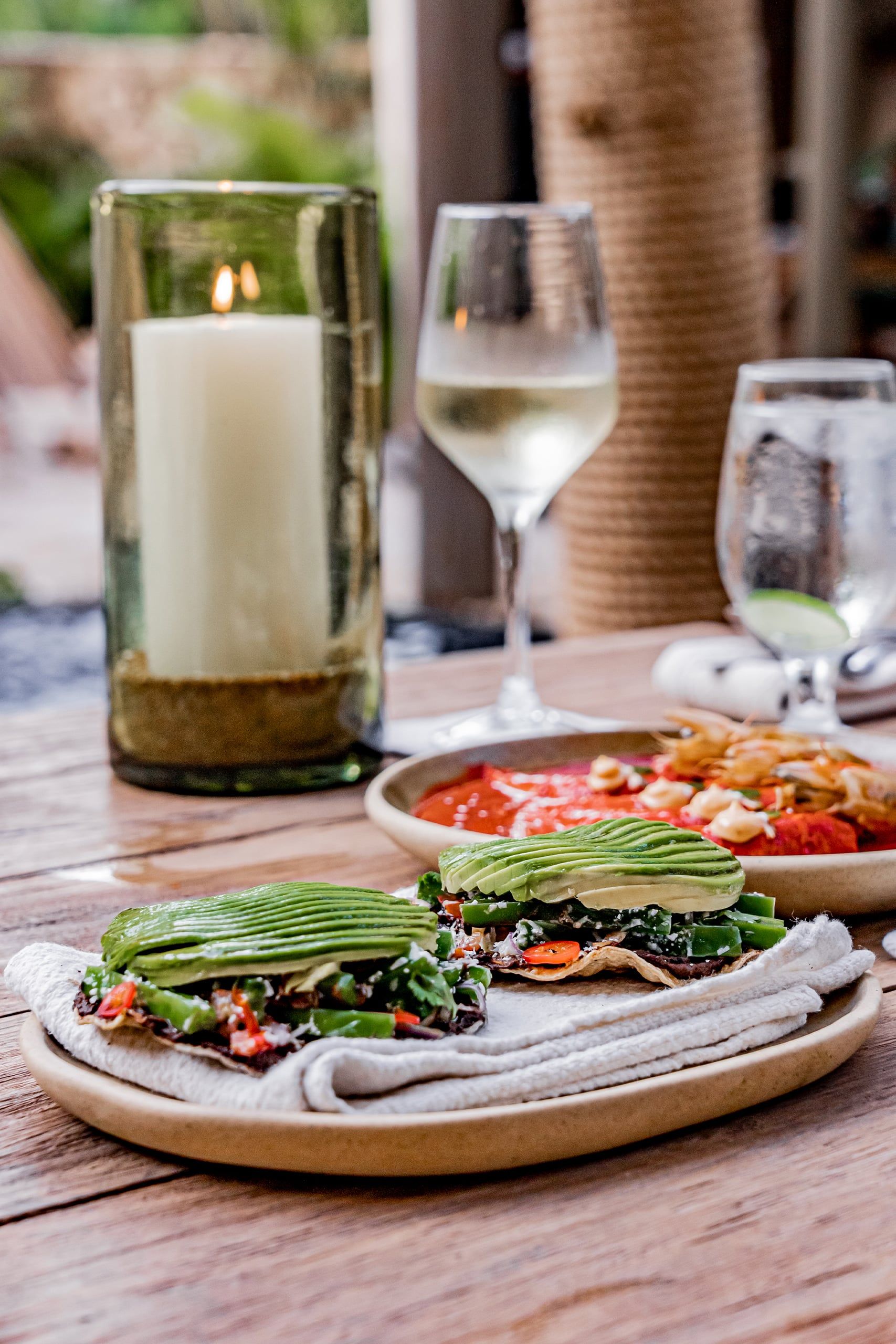Restaurant table with flatbread, green salad, a candle, and glasses of white wine