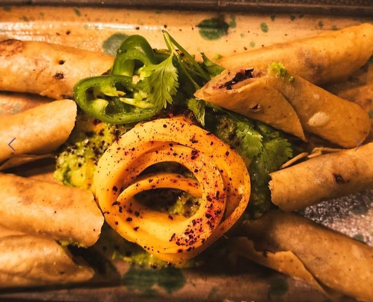 Assorted spring rolls arranged around a rose-shaped vegetable garnish with green herbs on a plate