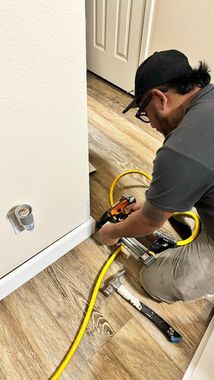 A man is kneeling down on the floor using a tool.