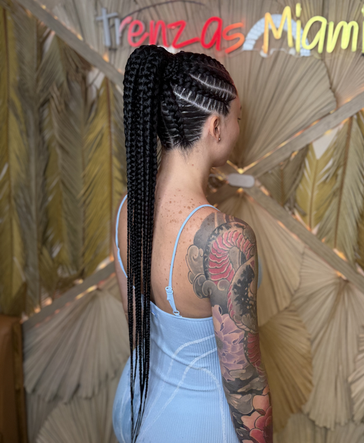 A woman with braids and a tattoo on her arm is wearing a blue dress.
