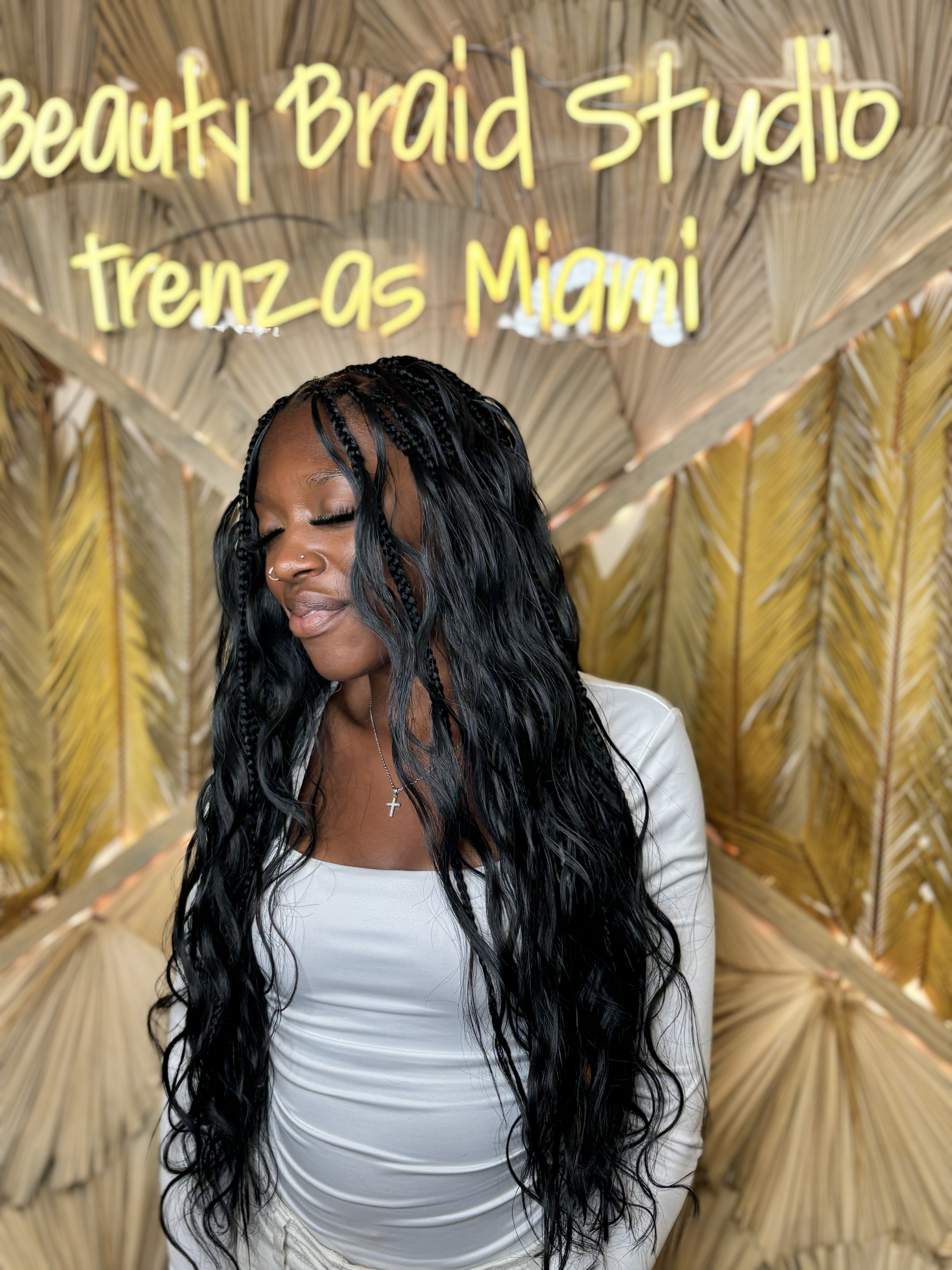 A woman with long black hair is standing in front of a palm tree.