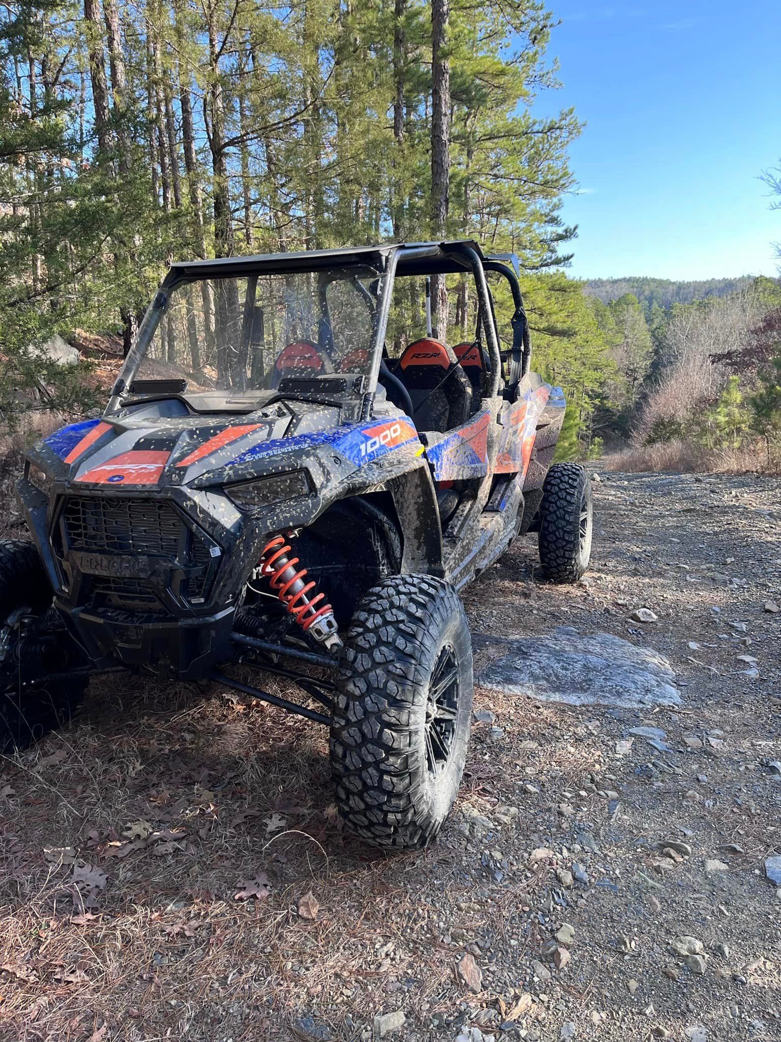 A blue and orange atv is parked on a dirt road in the woods.
