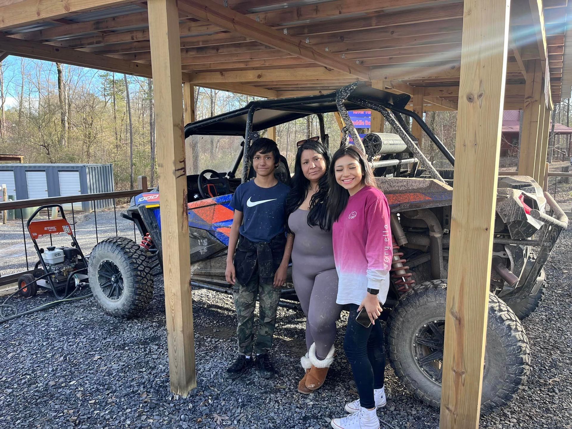 Three people are posing for a picture in front of a atv.