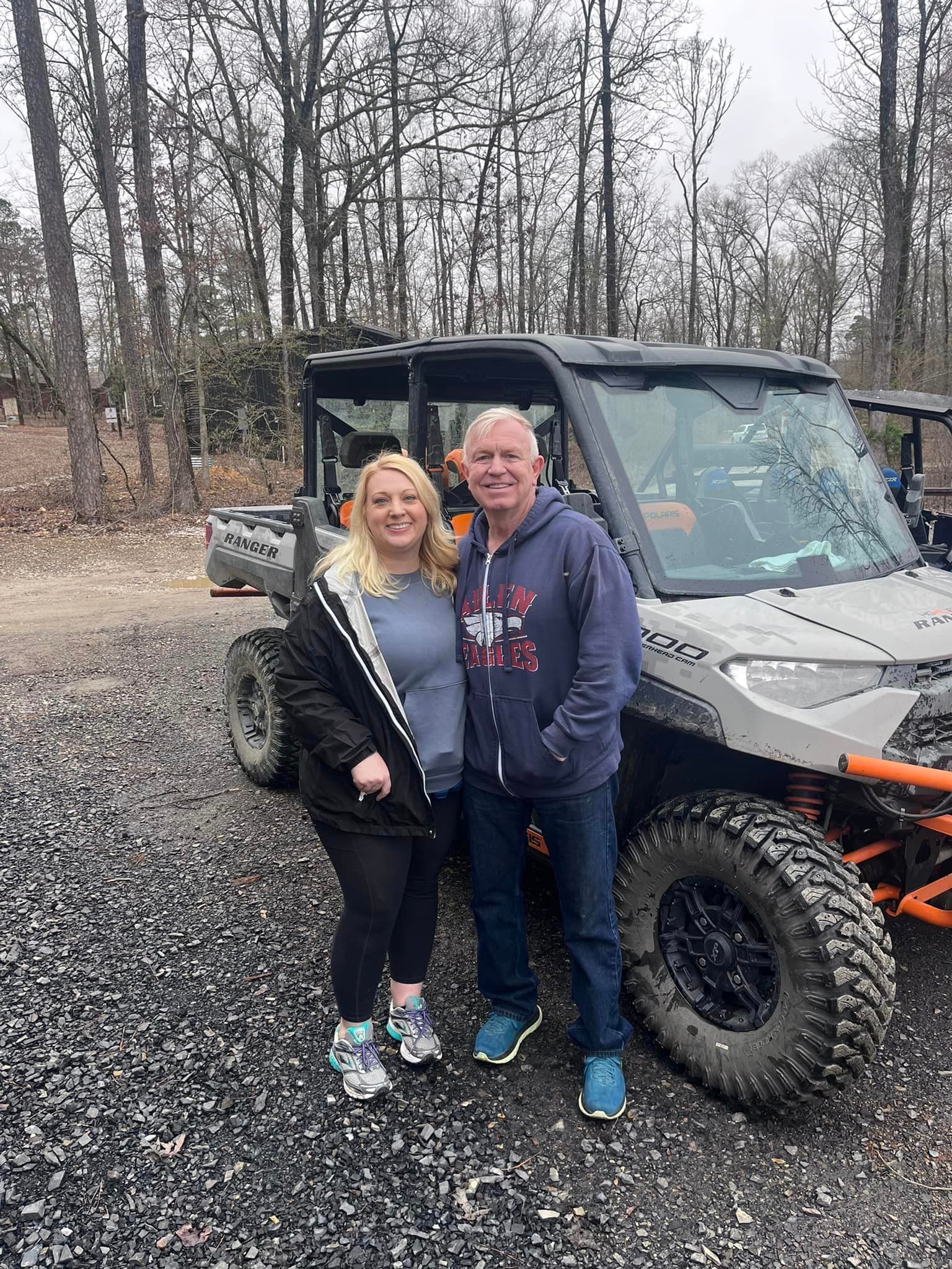 A man and a woman are standing in front of a atv.