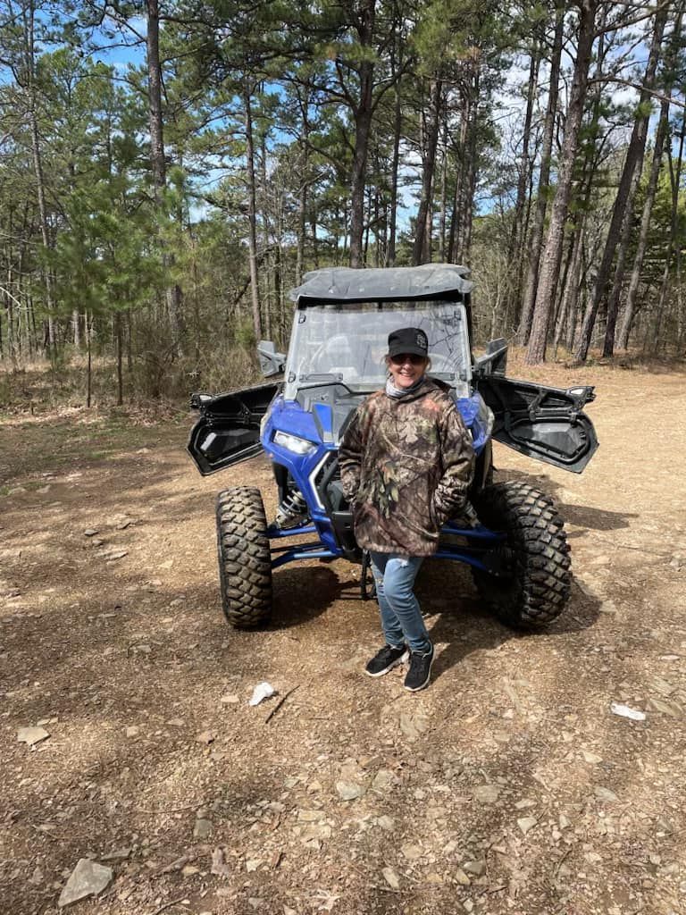 A man is standing in front of a atv in the woods.