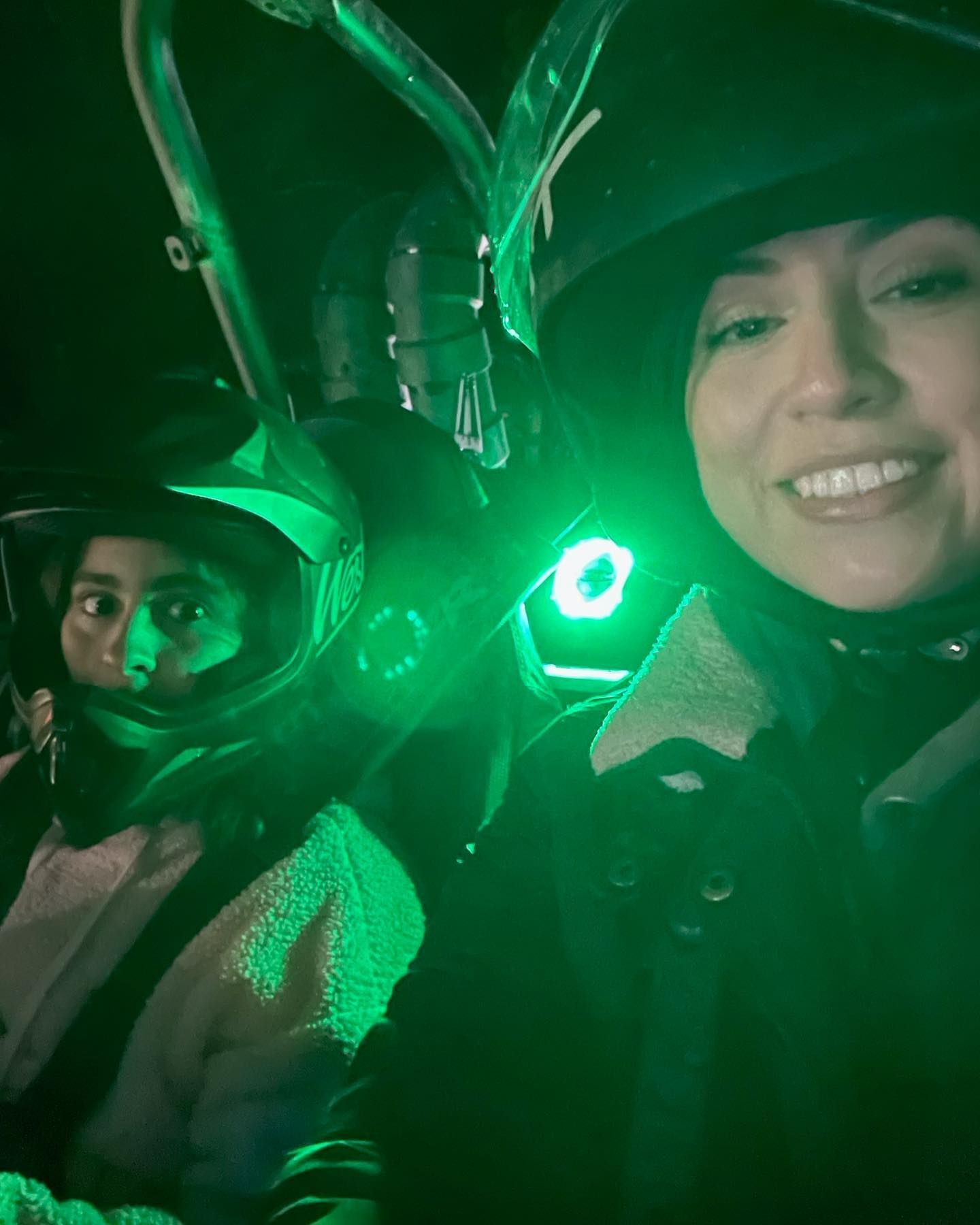 Two women wearing helmets are sitting in a car with a green light behind them.