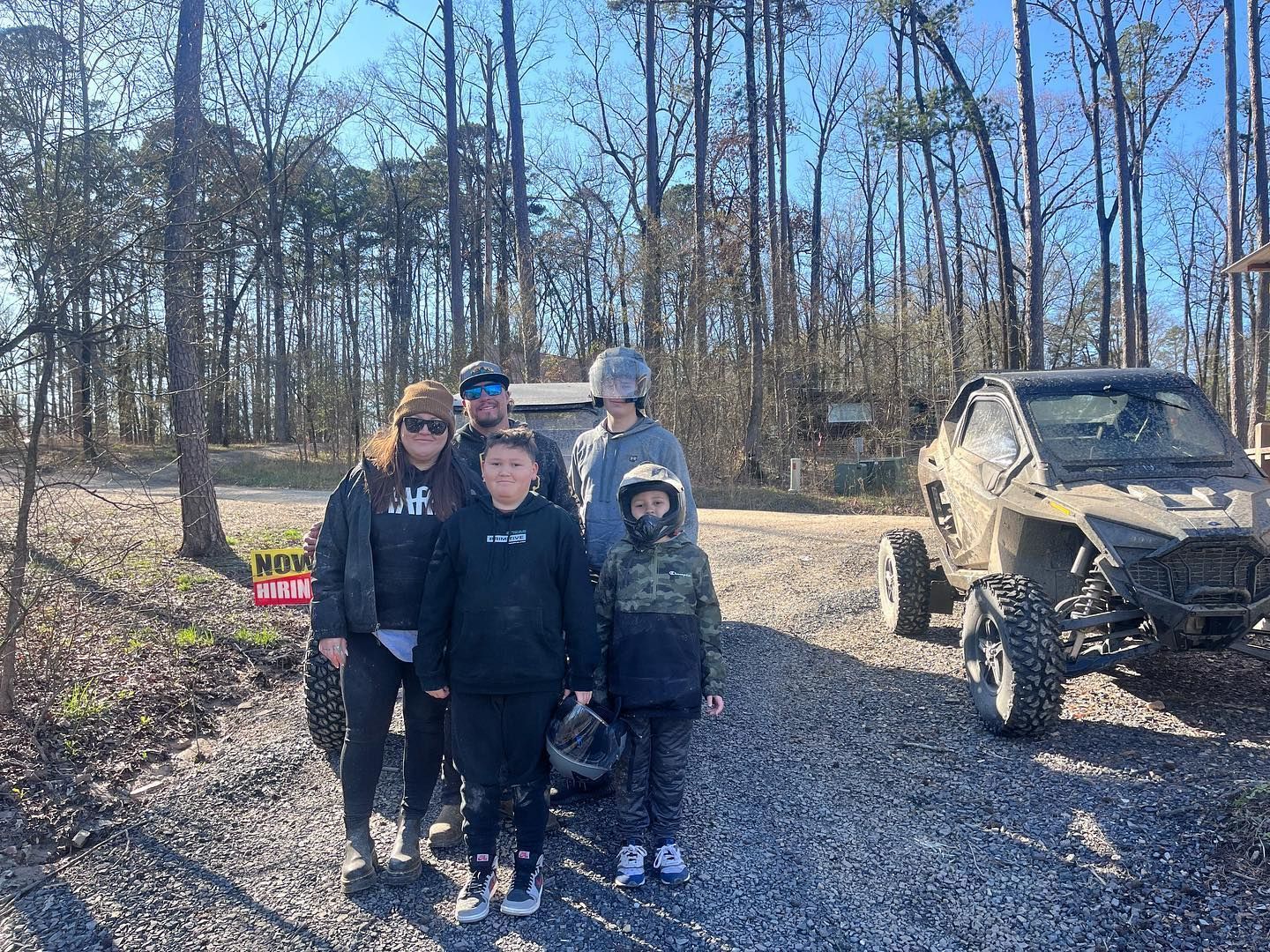 A family is posing for a picture in front of a atv in the woods.