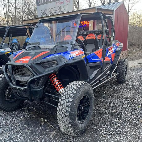 A blue and orange atv is parked in a gravel lot in front of a shed.