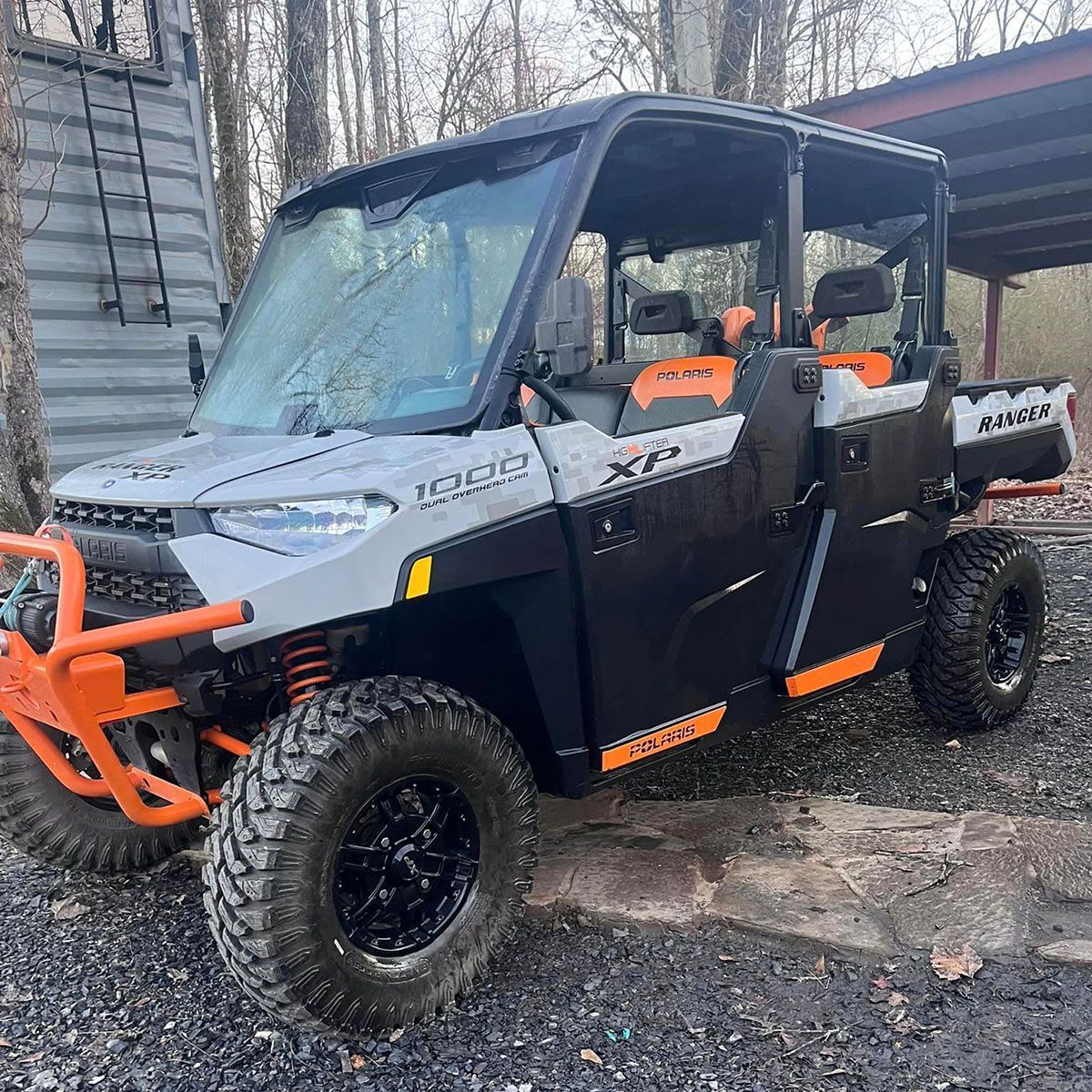 A polaris ranger xps is parked in a gravel lot in front of a building.