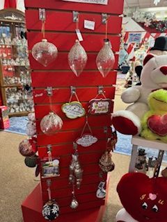 Christmas ornaments on a red display stand in a store. White plush toys are nearby.