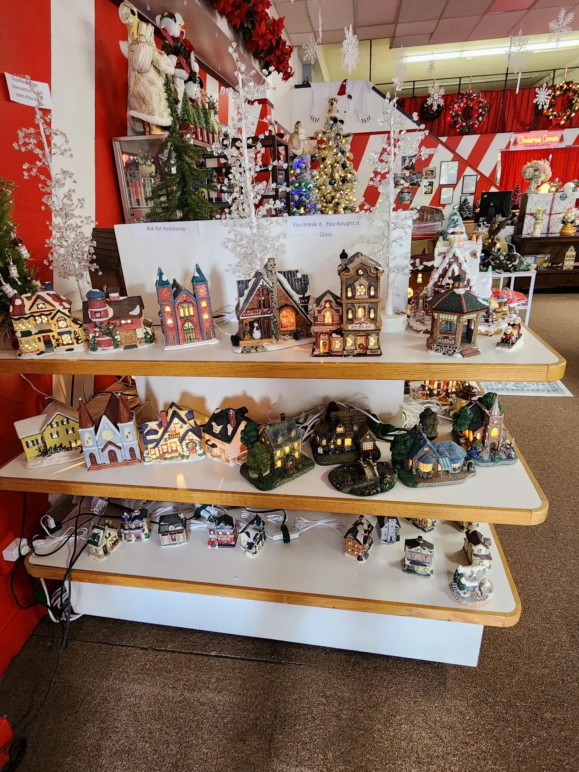 Shelves display illuminated Christmas village houses and decorations in a store.