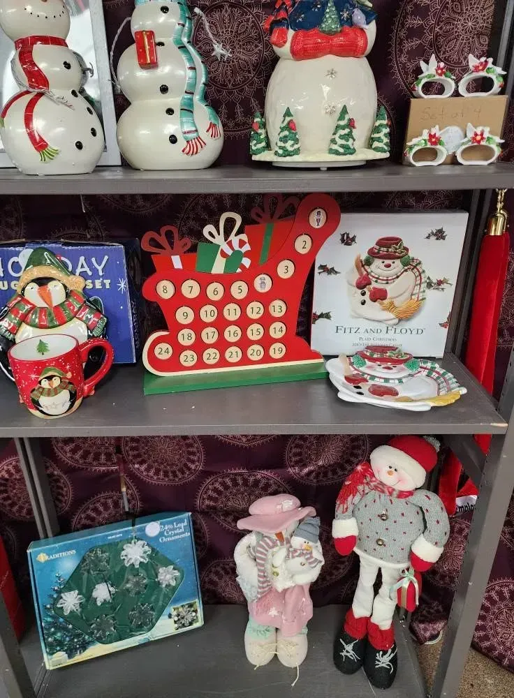 Christmas decorations on a shelf: snowmen, an advent calendar, a snowman-themed mug, and a plush doll.
