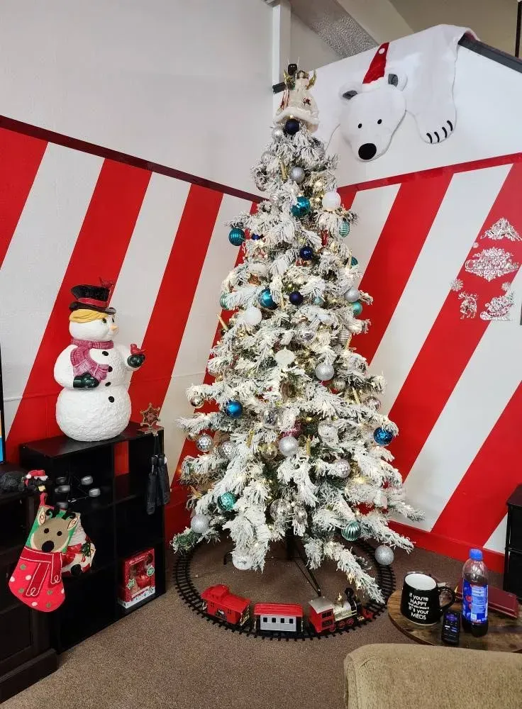 Christmas tree with decorations, snowman, train set, and a polar bear decoration against a red and white striped wall.