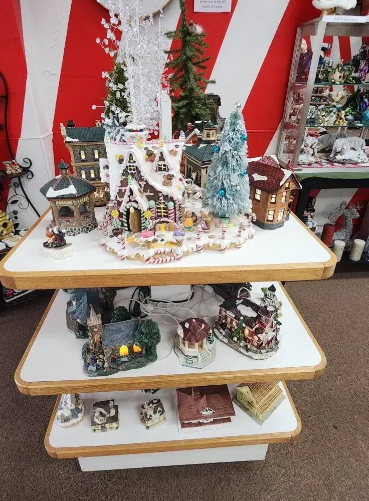 Three-tiered display of Christmas village figurines. Red and white striped backdrop.