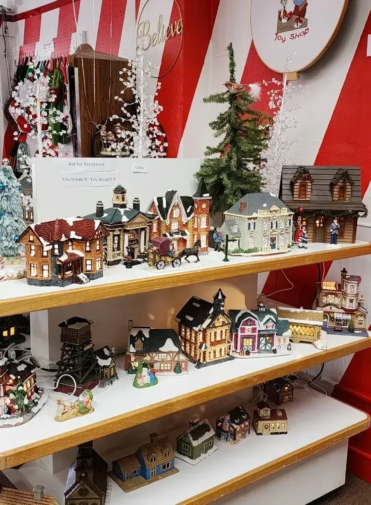 Shelves displaying a Christmas village collection with snow-covered buildings and a small Christmas tree.