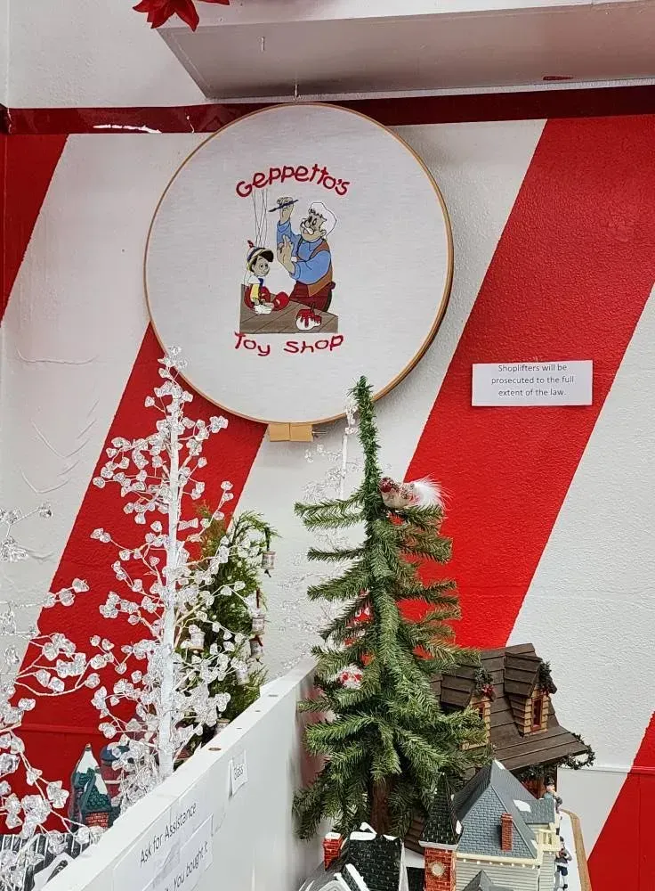 Circular embroidery of Gepetto's Toy Shop, displayed on a striped red and white wal.