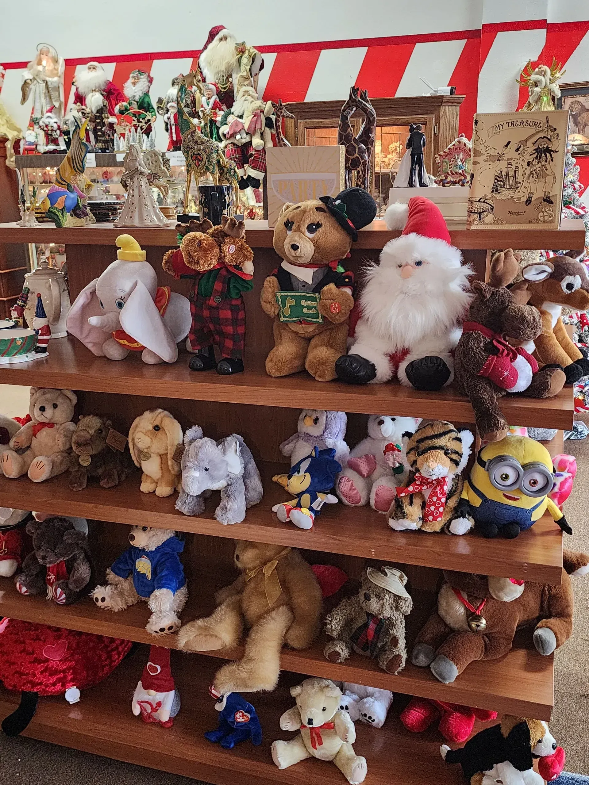 Shelves filled with various plush toys, including teddy bears and Santa figures. Red and white striped backdrop.