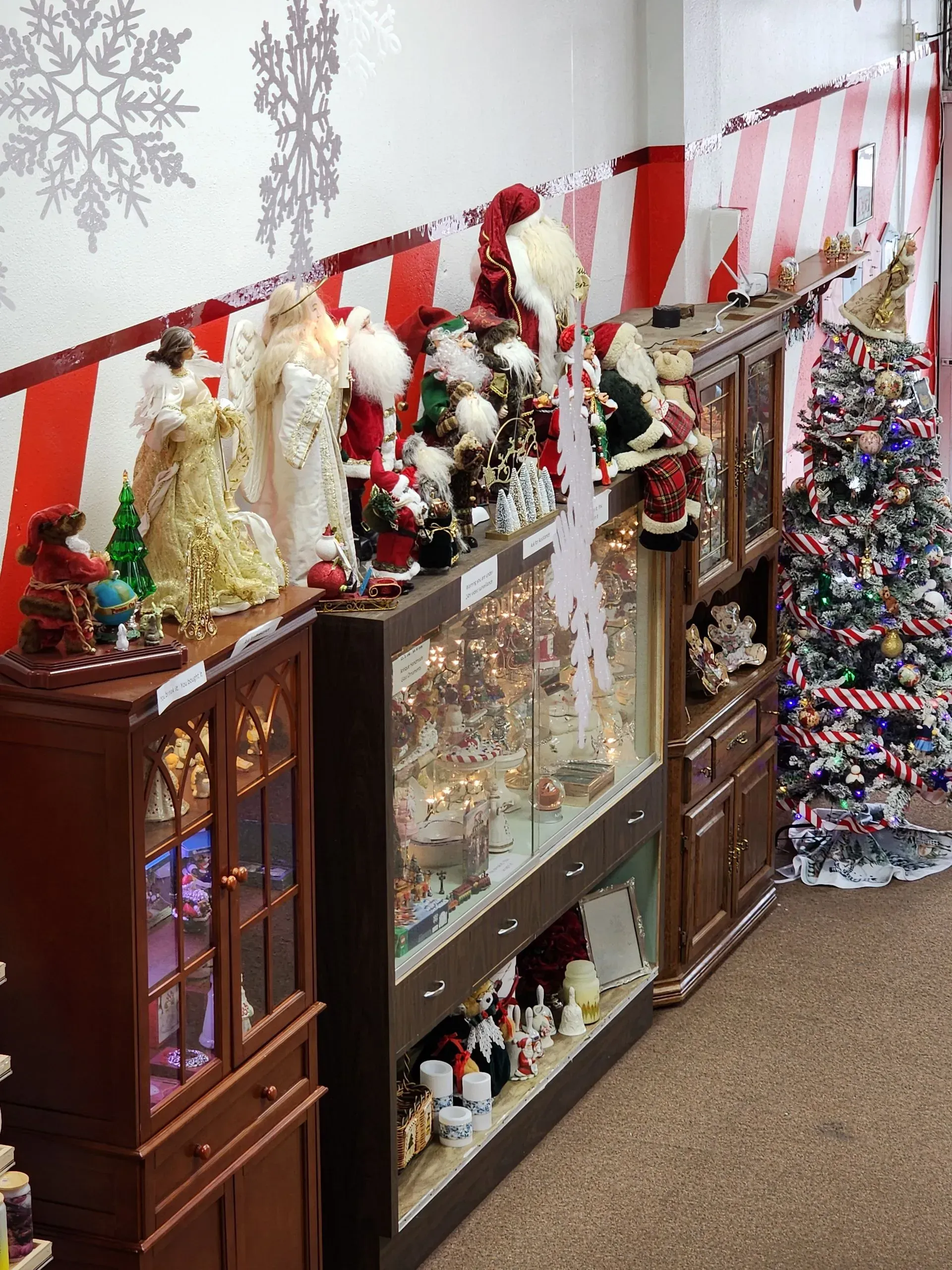Christmas decorations in a shop: Santas, angels, a tree, and red and white striped wall.