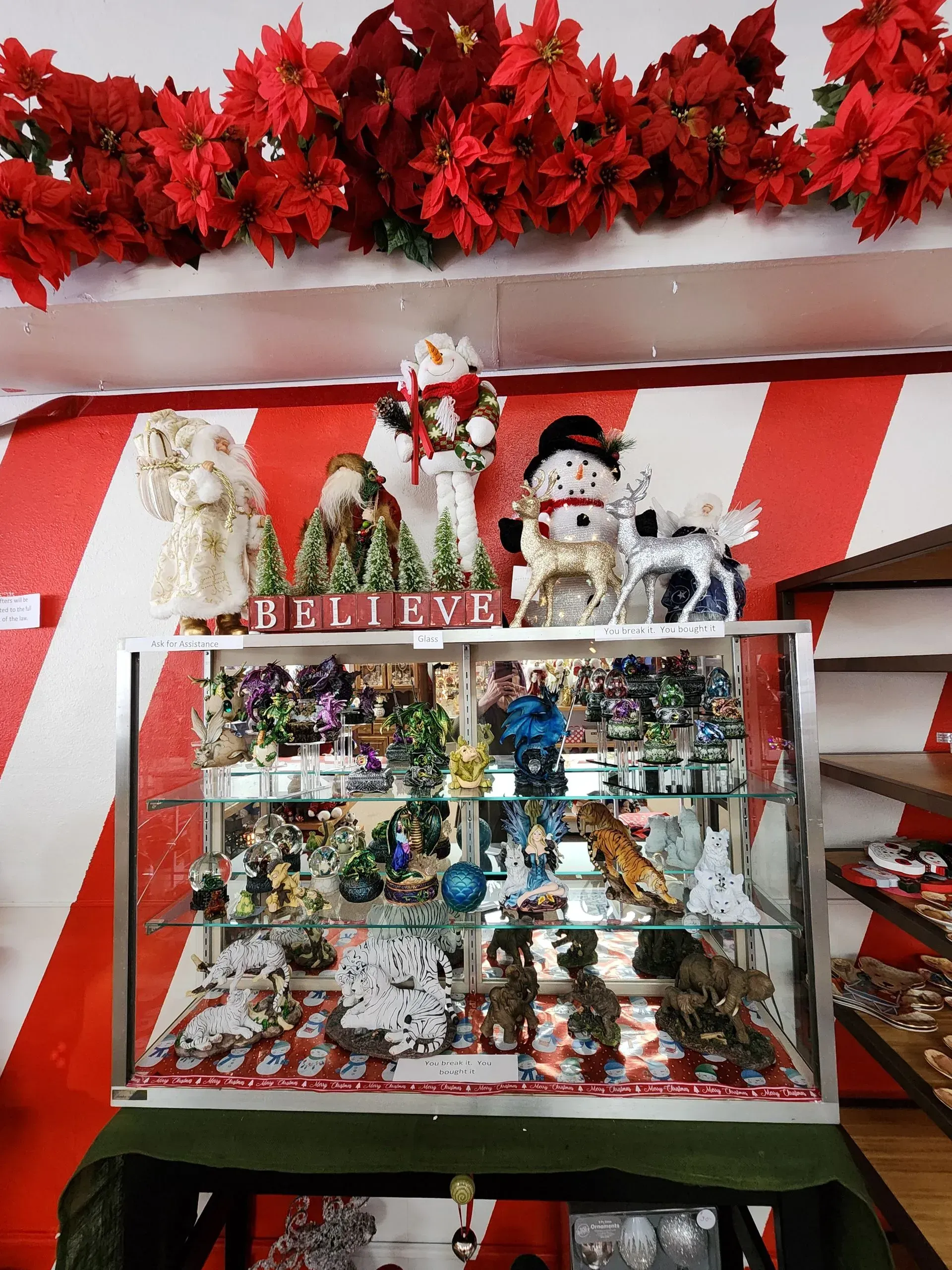 Christmas decorations in a display case; poinsettias above a red and white striped wall.