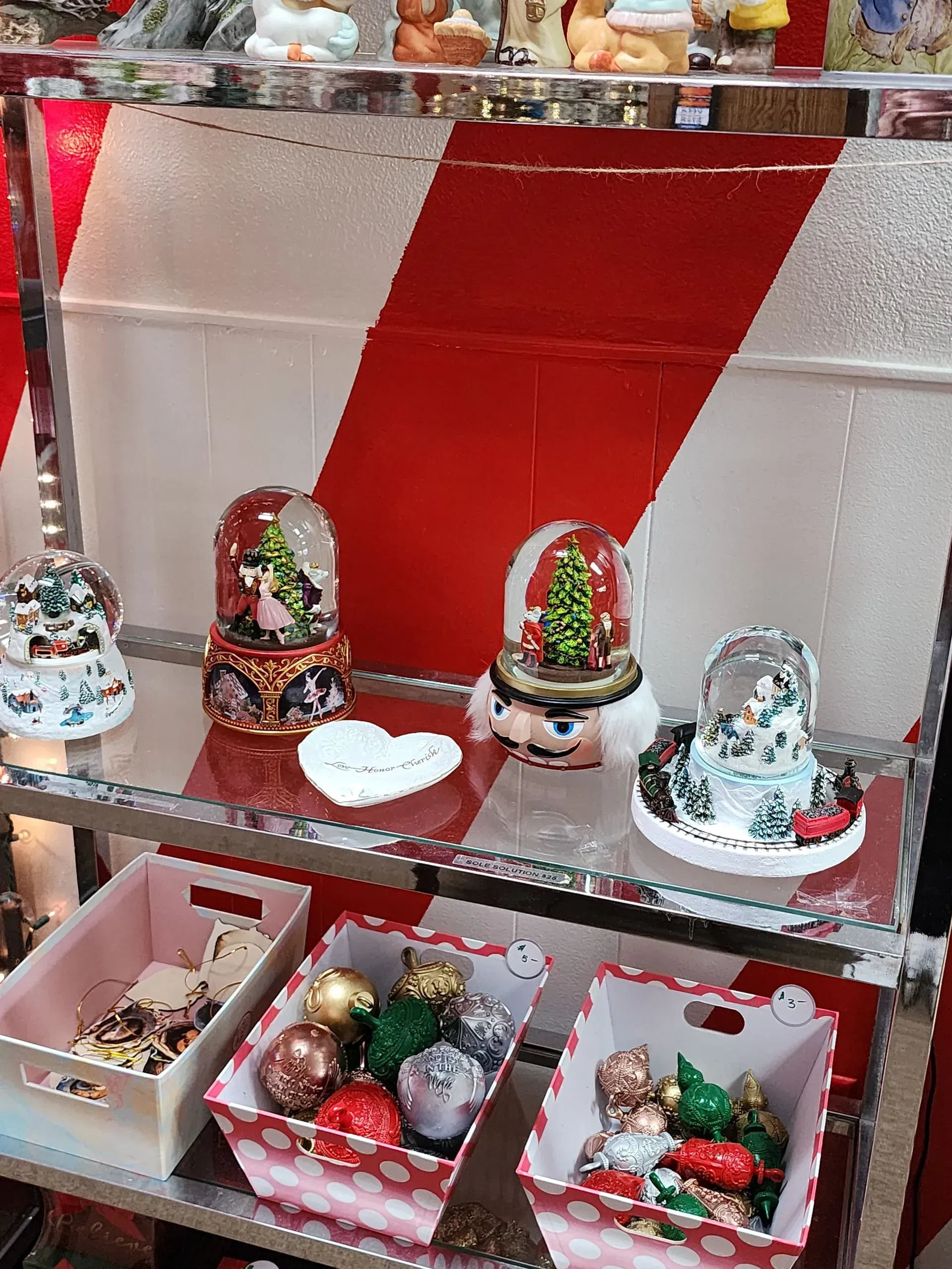 Christmas display with snow globes, ornaments, and storage boxes; red and white colors.