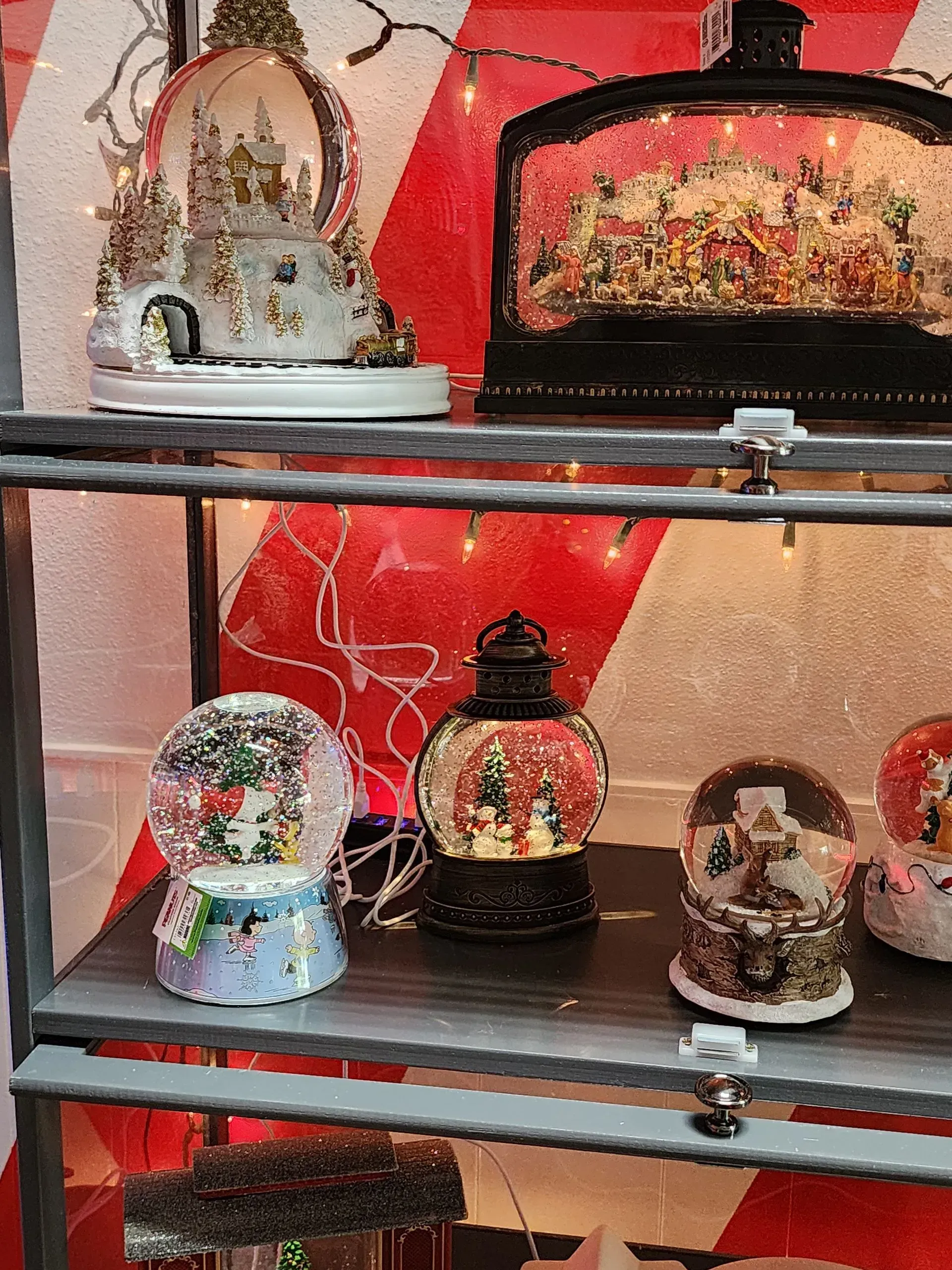 Christmas snow globes displayed on shelves, against a red and white striped background.