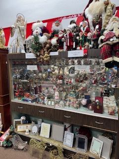 Display case filled with Santa figurines and Christmas ornaments. Brown wooden cabinet.