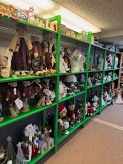 Green shelving filled with teddy bears, dolls, and figurines in a well-lit room.