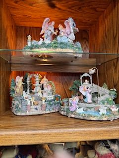 Three angel figurines on wooden shelves; detailed garden settings, pastel colors.