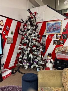 Christmas tree in a room with red and white striped walls, snowman, framed pictures, and a blue ottoman.
