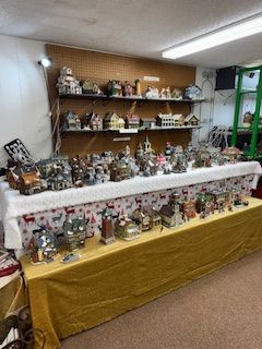 A display of miniature village houses and figurines on tables and shelves indoors.