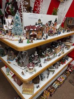 Shelves display Christmas village houses, figurines, and a snowy tree, set against a candy-cane-striped backdrop.