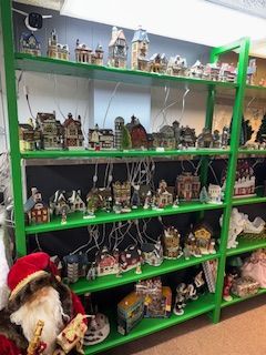 Green shelves hold a Christmas village display with lighted buildings and Santa Claus on the side.