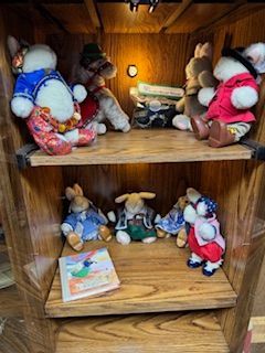 Wooden cabinet with stuffed rabbits on shelves; some wearing clothes.