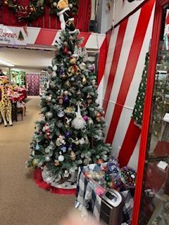 Christmas tree with ornaments in a store, next to a red and white striped wall.