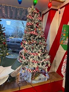 Christmas tree with red and white ribbon and ornaments.  Inside a shop window with red and white striped wall.