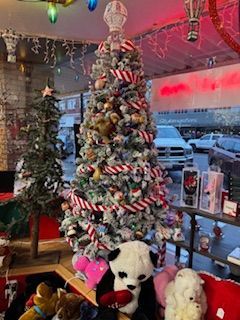 Christmas tree decorated with red and white ribbon and ornaments, panda plush toy, inside a store.