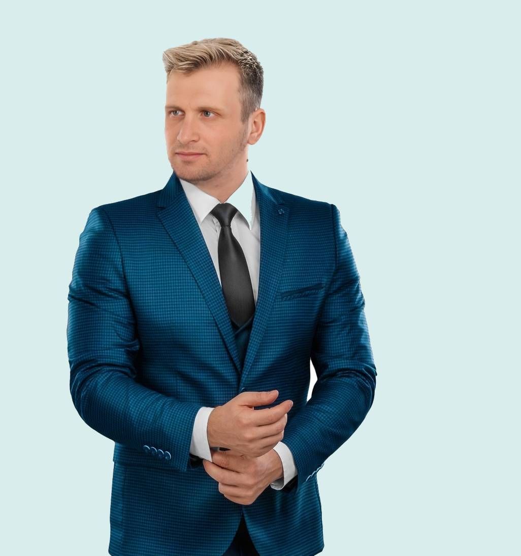 A man in a blue suit and tie is standing with his hands folded