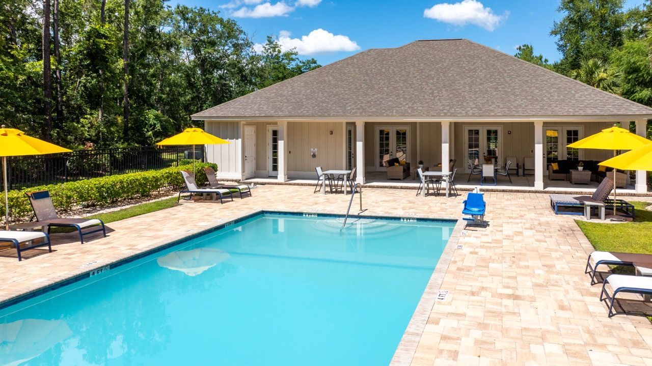 Outdoor pool area with lounge chairs, yellow umbrellas, and a clubhouse building.