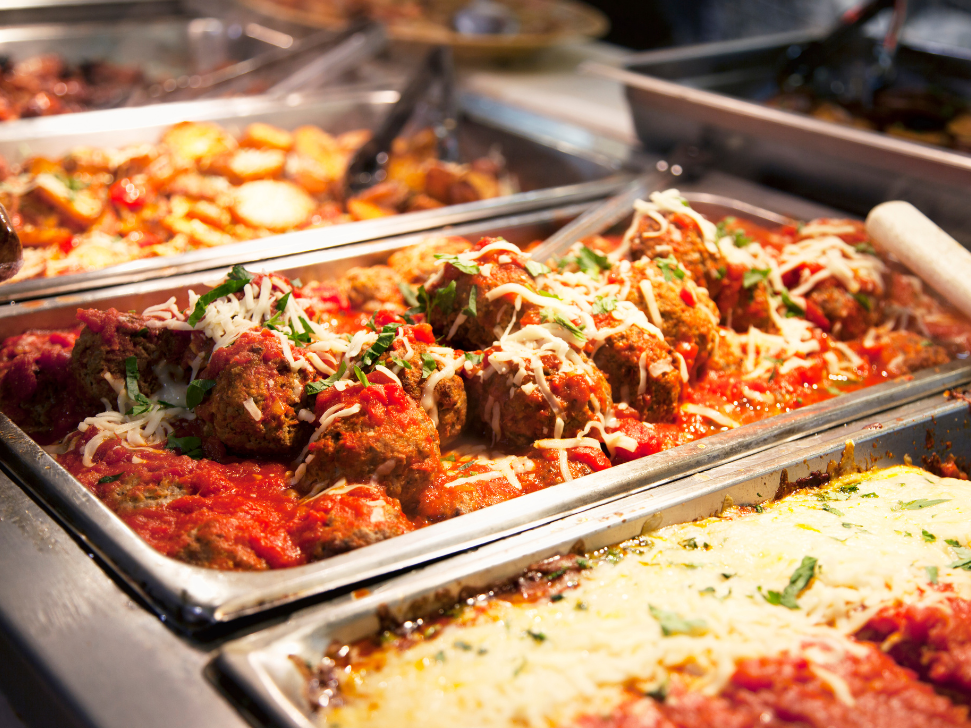Buffet trays with meatballs in red sauce and other dishes.