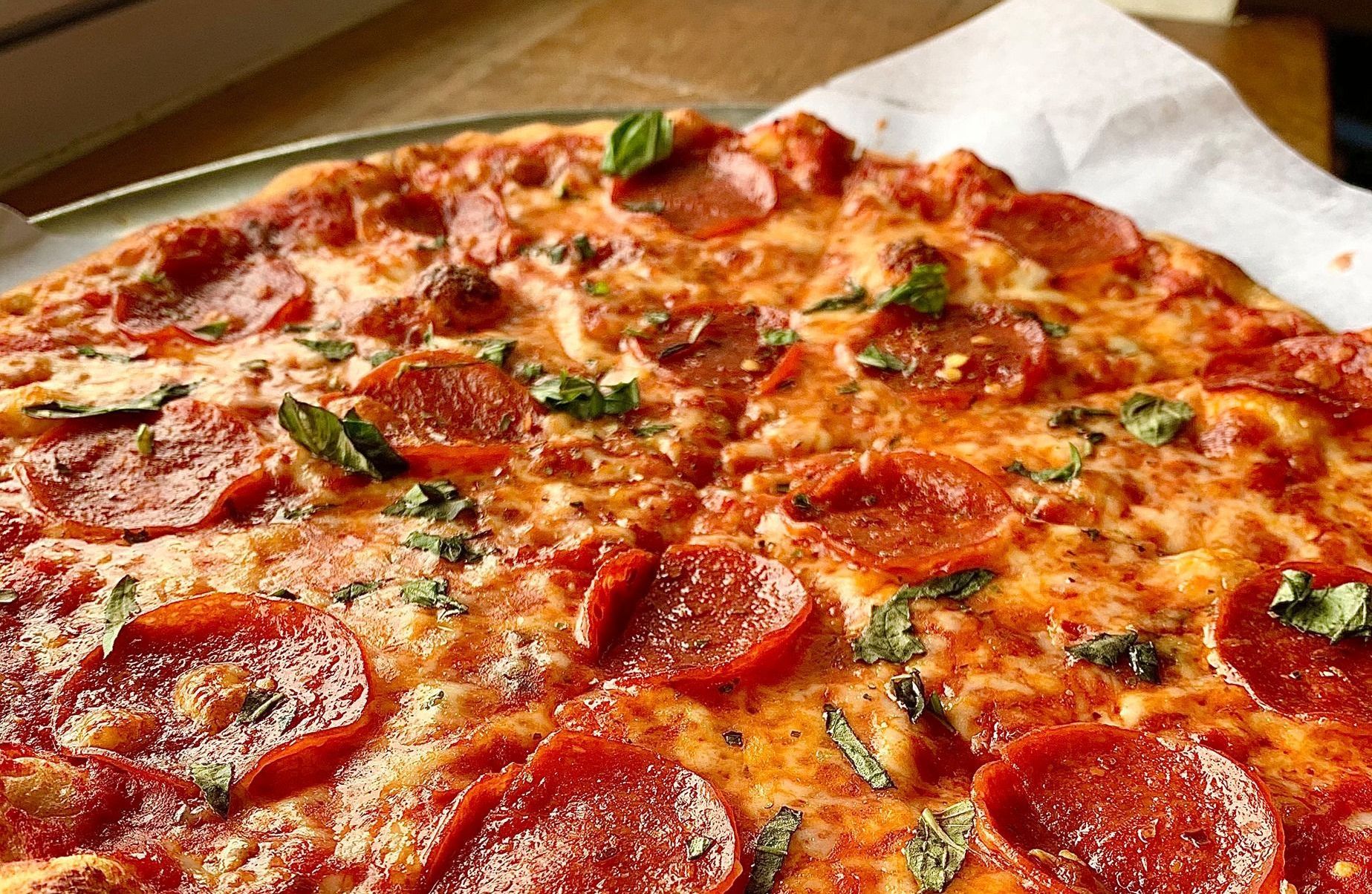 A margherita pizza with tomatoes, mozzarella cheese and basil on a metal pan.