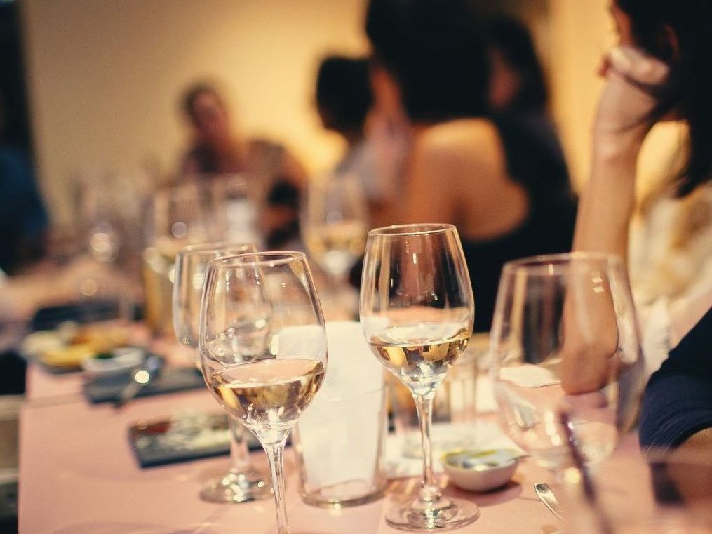 Wine glasses on a table at a restaurant with people in the background, dimly lit.