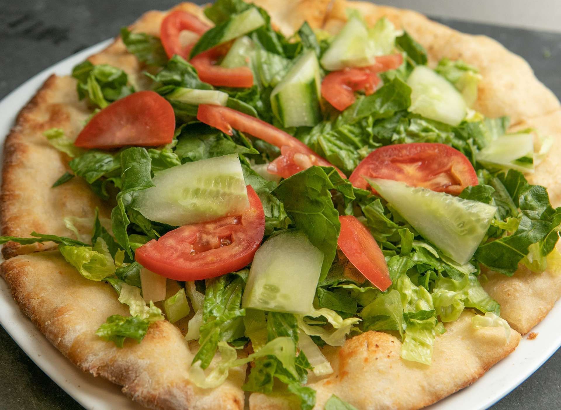 A margherita pizza with tomatoes, mozzarella cheese and basil on a metal pan.