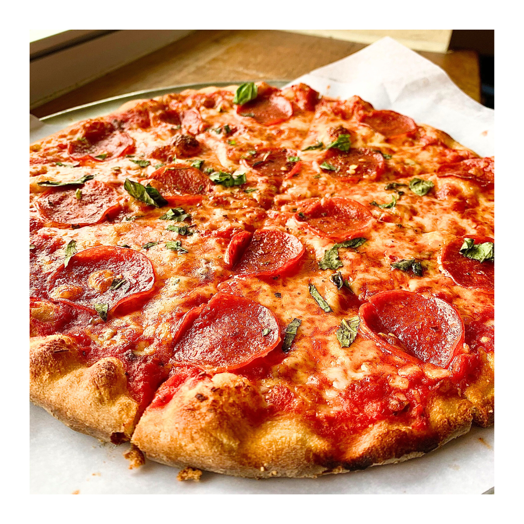 Pepperoni pizza on parchment paper, crusty golden, sliced, with basil.