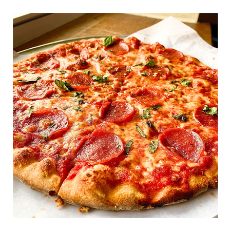 Pepperoni pizza on parchment paper, crusty golden, sliced, with basil.