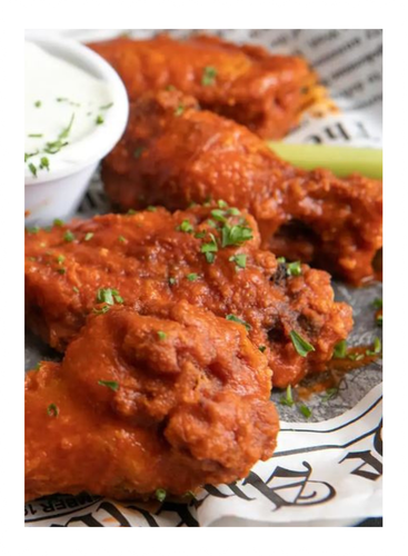 Close-up of crispy, red buffalo wings with blue cheese dip and a celery stick.