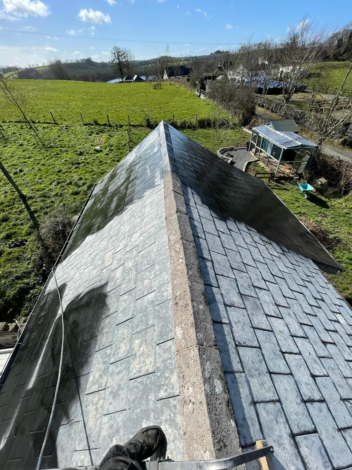View from a roof of dark grey slate tiles, a green field, and a bright blue sky.