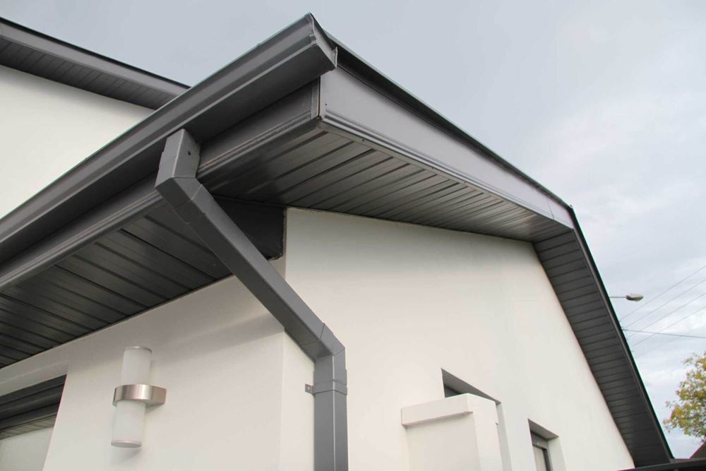 Gray gutters and trim on a white house under a cloudy sky.