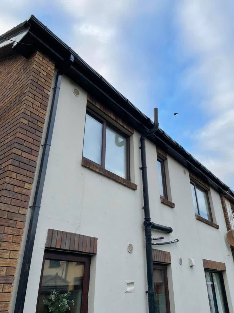 Man on ladder fixing gutter on brick house.