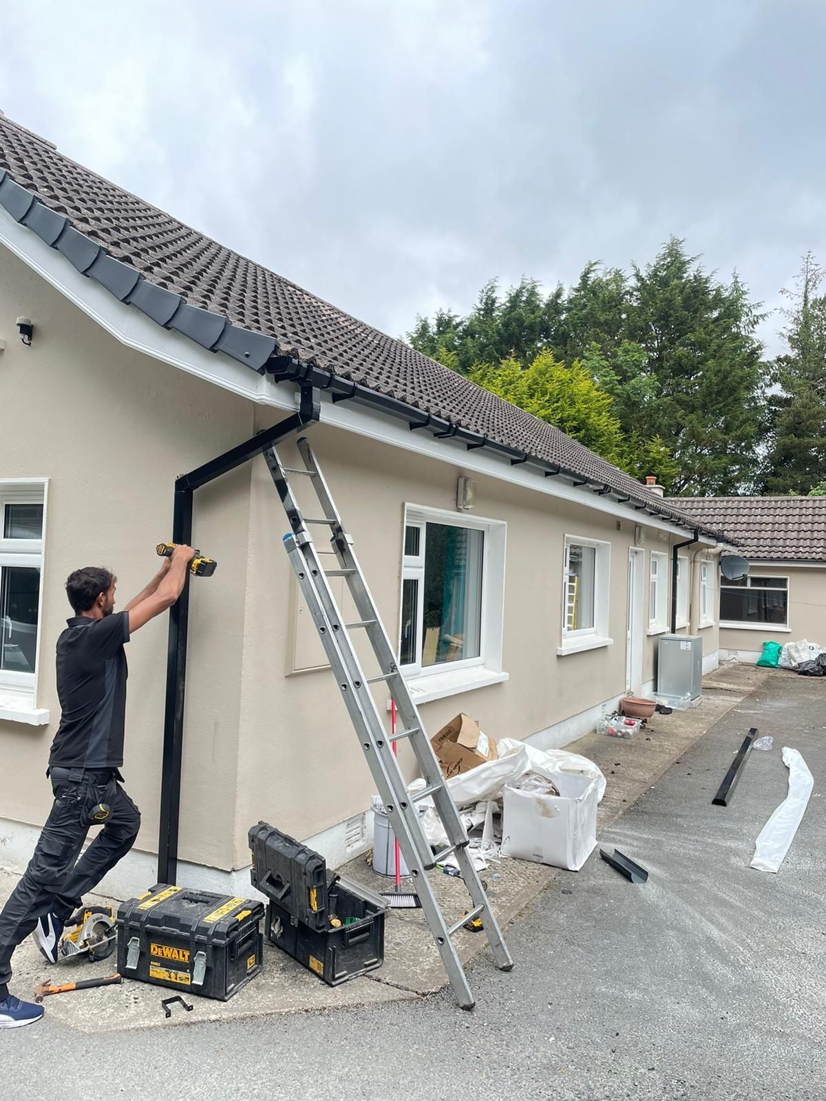 Two workers on scaffolding installing guttering on a brick house. Sunny, blue sky.